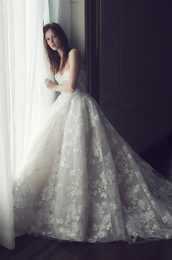 Woman wearing Monique Lhuillier Fall 2019 white and blush strapless Easton ball gown with embroidered floral lace applique
